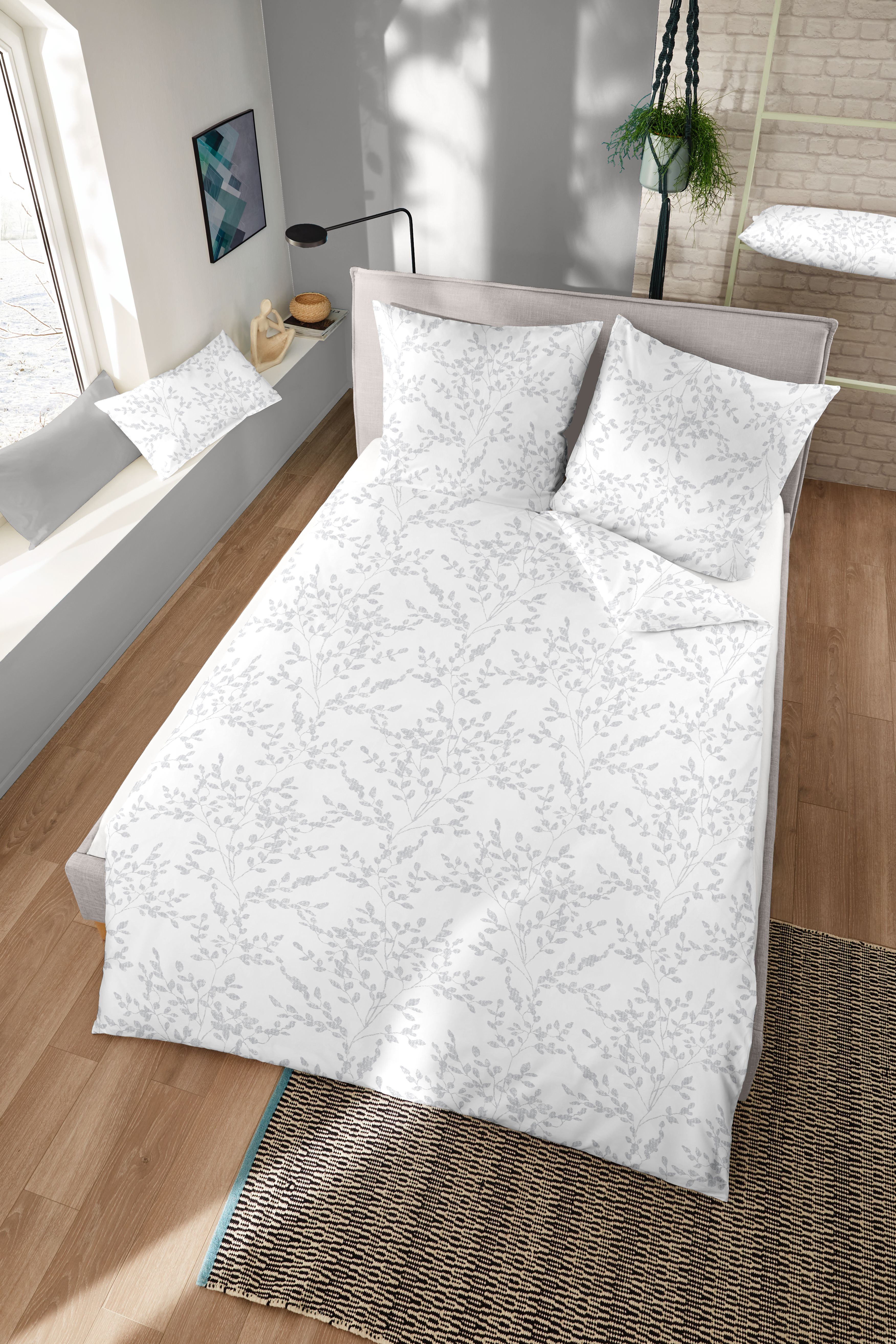 Kuschelige weiße Edelbiberbettwäsche mit grauen dezenten Blättermotiven bezogen auf ein Bett